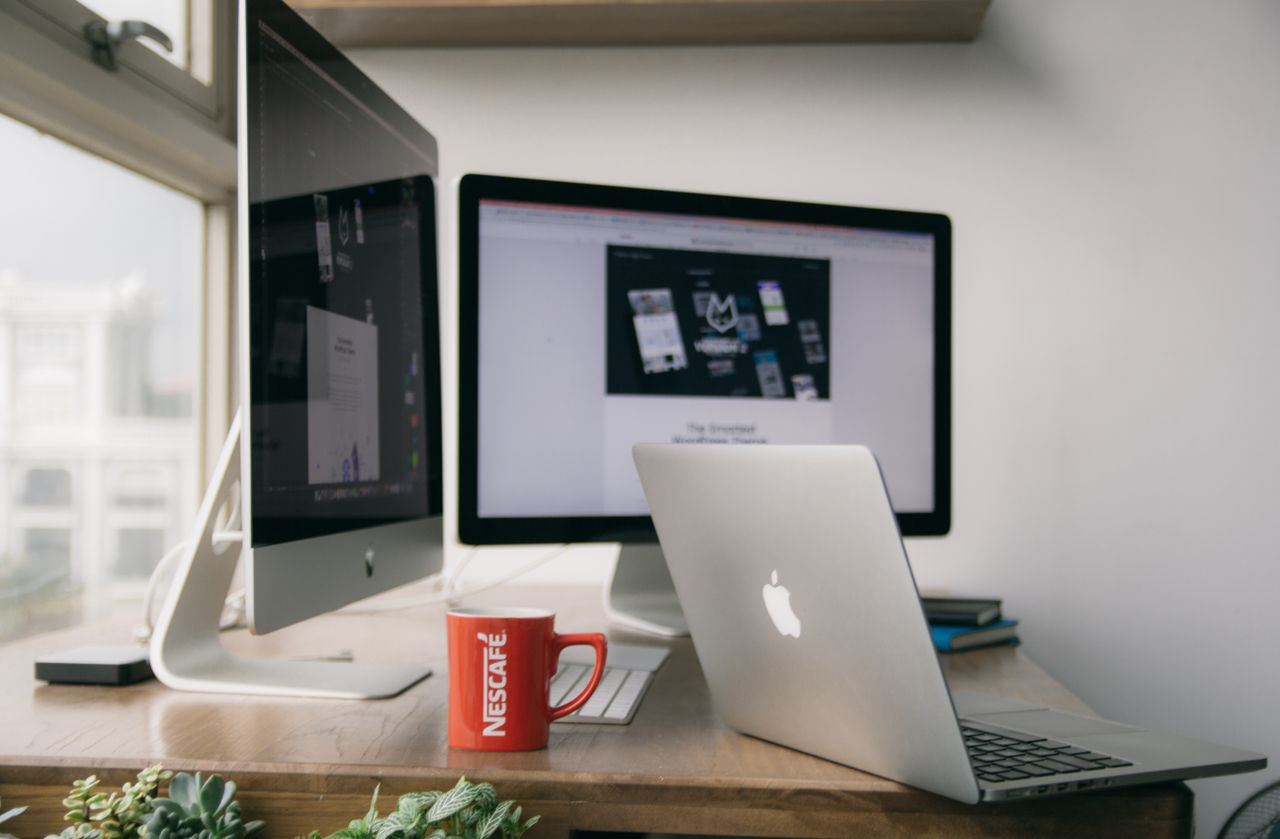 A bright, contemporary office arrangement with computers and a mug sitting on a desk.